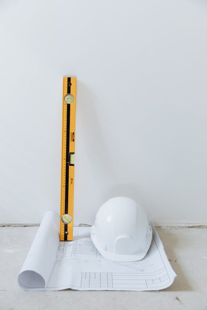 Rolled blueprint, hard hat, and level tool arranged against a white background.